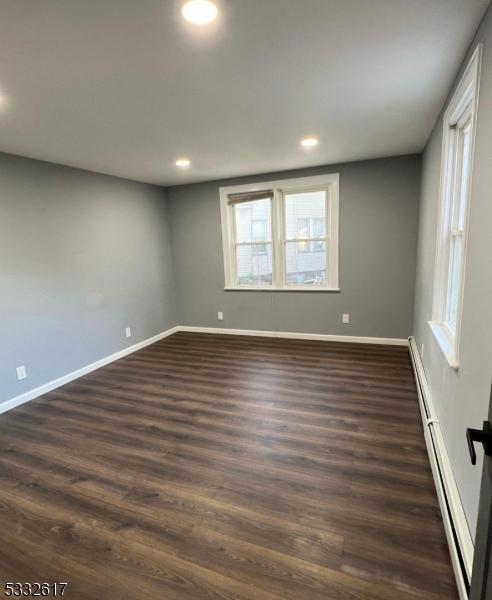 empty room with dark hardwood / wood-style flooring and a baseboard heating unit