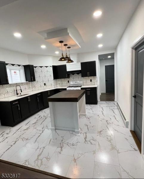 kitchen featuring hanging light fixtures, white range, a kitchen island, a baseboard heating unit, and sink