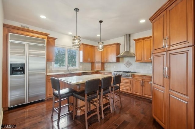 kitchen with a kitchen island, decorative light fixtures, sink, stainless steel appliances, and wall chimney range hood