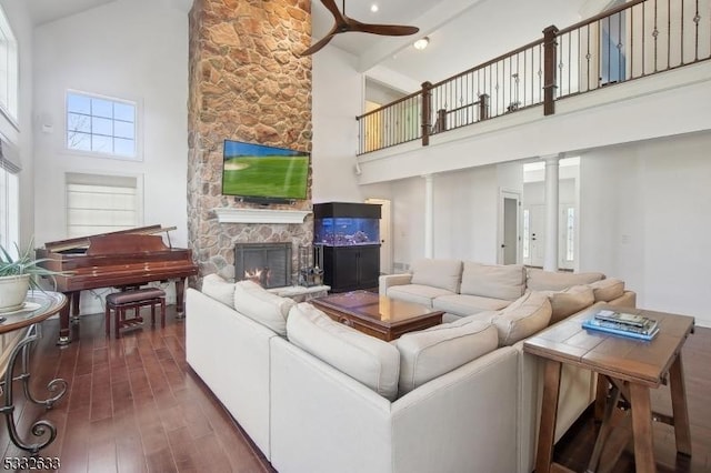 living room featuring ceiling fan, high vaulted ceiling, decorative columns, dark hardwood / wood-style flooring, and a stone fireplace