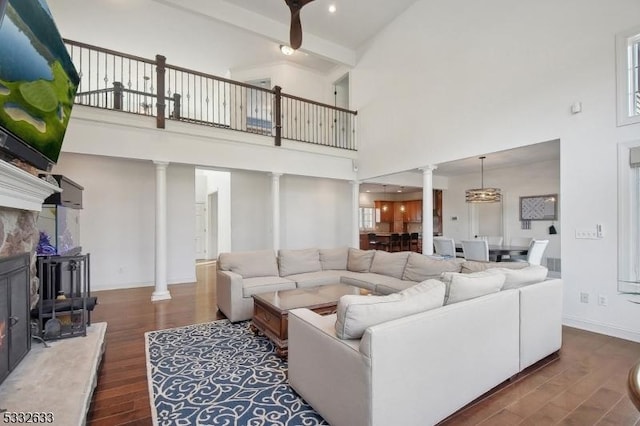 living room with beam ceiling, a towering ceiling, dark wood-type flooring, and decorative columns