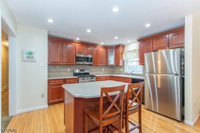 kitchen with light hardwood / wood-style floors, a breakfast bar area, decorative backsplash, a kitchen island, and appliances with stainless steel finishes