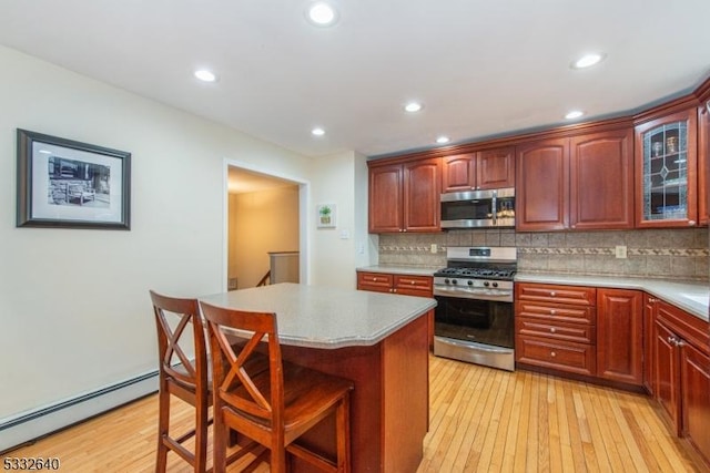 kitchen featuring stainless steel appliances, baseboard heating, a kitchen breakfast bar, light hardwood / wood-style floors, and a kitchen island