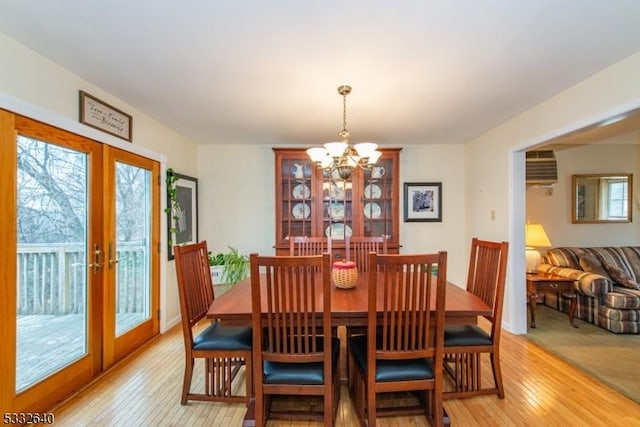 dining room featuring a wall mounted air conditioner, a notable chandelier, light hardwood / wood-style floors, and french doors