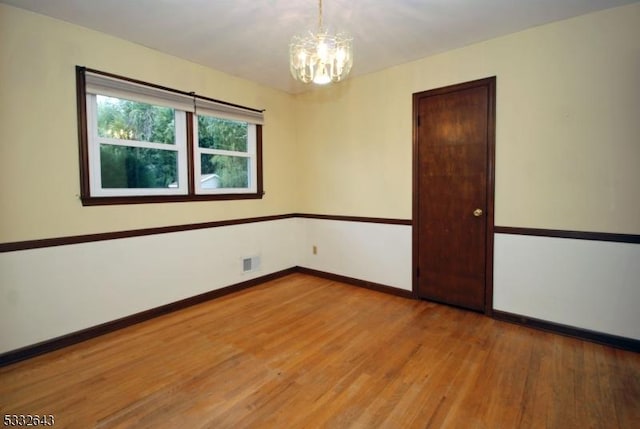 empty room featuring light wood-type flooring and a notable chandelier