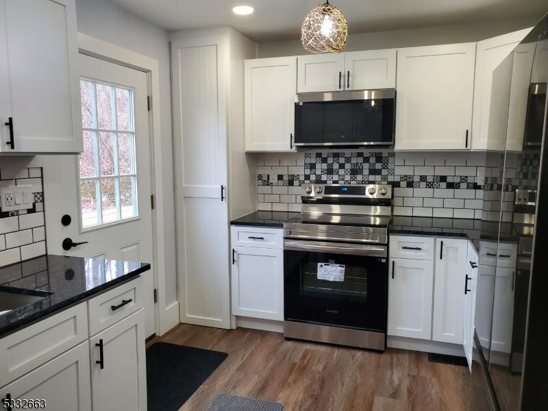 kitchen with pendant lighting, appliances with stainless steel finishes, hardwood / wood-style flooring, white cabinetry, and decorative backsplash