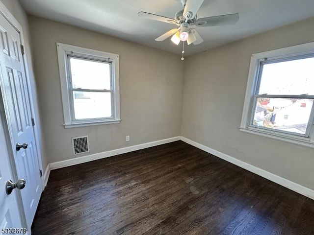 spare room with dark hardwood / wood-style flooring, ceiling fan, and a healthy amount of sunlight