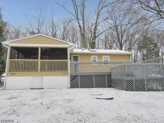 snow covered rear of property featuring a wooden deck and a sunroom