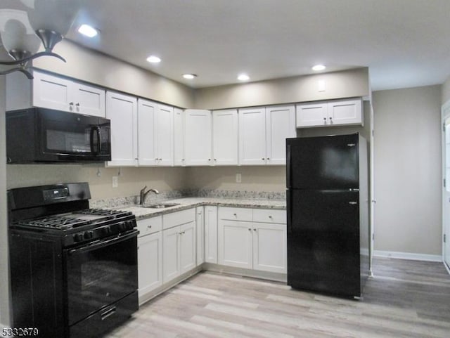 kitchen featuring light wood-type flooring, light stone counters, sink, black appliances, and white cabinetry