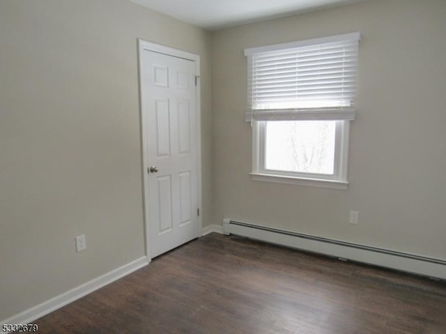 empty room featuring dark wood-type flooring and a baseboard heating unit