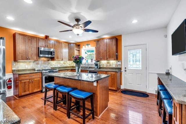 kitchen with a kitchen bar, light hardwood / wood-style floors, appliances with stainless steel finishes, and dark stone countertops