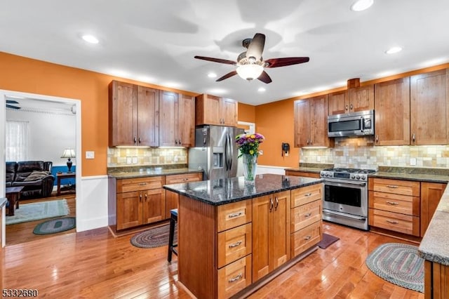 kitchen with dark stone countertops, appliances with stainless steel finishes, light wood-type flooring, and a kitchen island