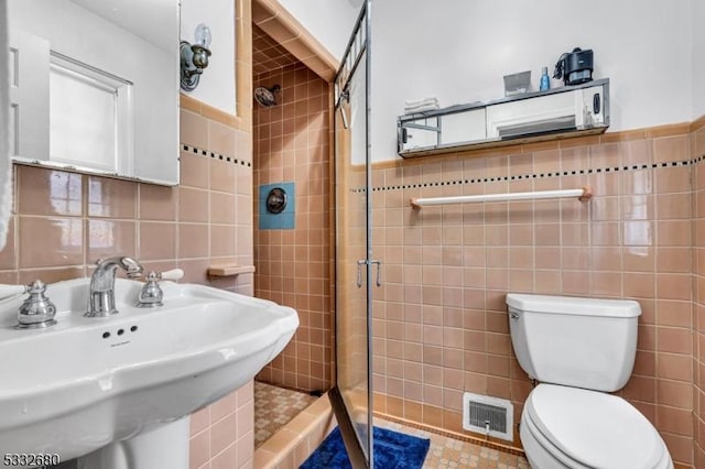 bathroom featuring toilet, a tile shower, tile walls, and sink