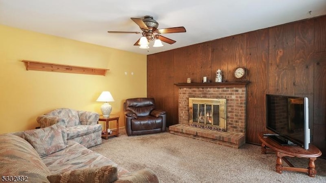 carpeted living room featuring ceiling fan, wood walls, and a fireplace