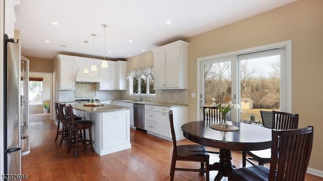 kitchen with a center island, stainless steel appliances, hanging light fixtures, decorative backsplash, and white cabinetry