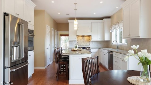 kitchen with pendant lighting, high end appliances, white cabinets, a kitchen island, and light stone countertops