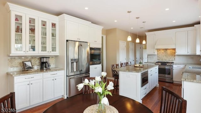 kitchen with decorative light fixtures, stainless steel appliances, glass insert cabinets, white cabinets, and premium range hood