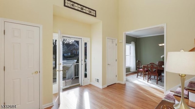 interior space with light wood finished floors, visible vents, baseboards, a high ceiling, and crown molding