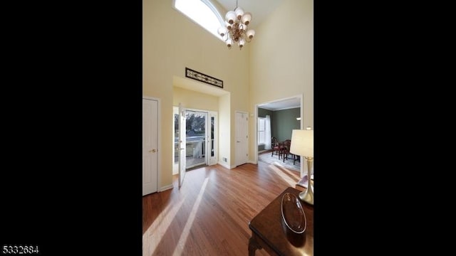 foyer featuring wood finished floors, a towering ceiling, baseboards, and an inviting chandelier