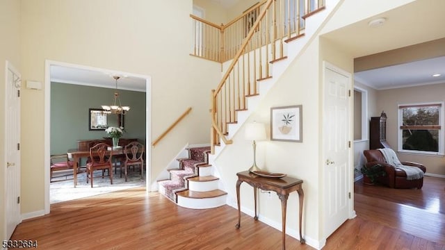 staircase featuring a chandelier, ornamental molding, a towering ceiling, and wood finished floors