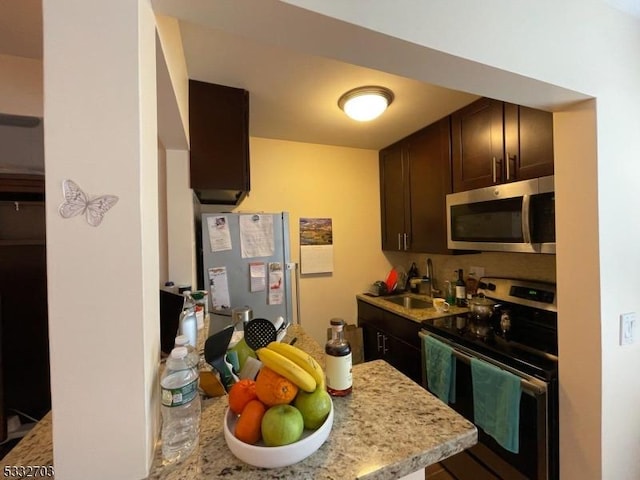 kitchen featuring appliances with stainless steel finishes, dark brown cabinets, light stone countertops, and sink