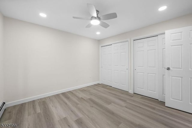 unfurnished bedroom featuring two closets, ceiling fan, a baseboard radiator, and light hardwood / wood-style floors