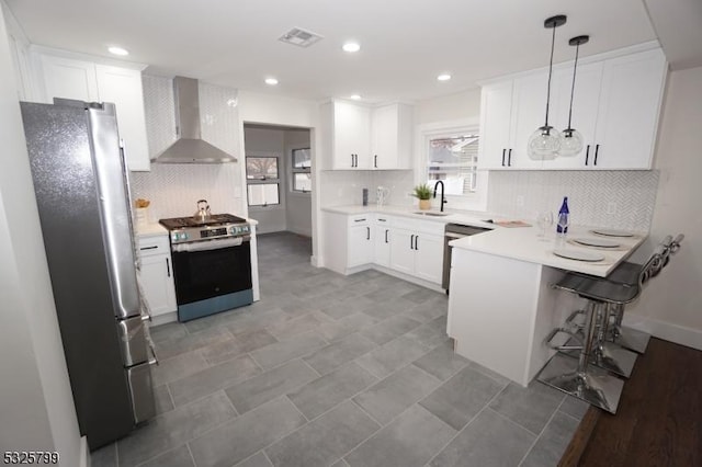 kitchen with wall chimney exhaust hood, stainless steel appliances, sink, decorative light fixtures, and white cabinetry