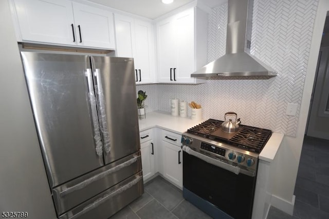 kitchen featuring tasteful backsplash, stainless steel appliances, wall chimney range hood, dark tile patterned flooring, and white cabinets