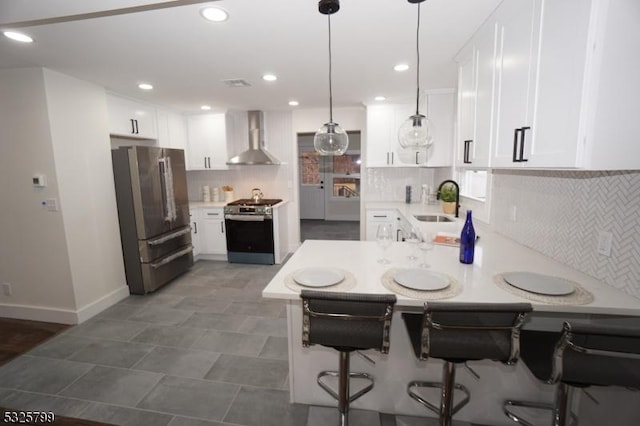 kitchen featuring kitchen peninsula, stainless steel appliances, wall chimney range hood, pendant lighting, and white cabinets