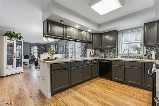 kitchen with kitchen peninsula, light wood-type flooring, black dishwasher, and sink