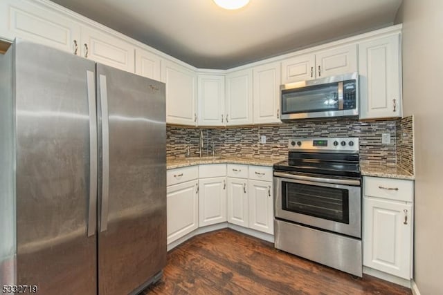 kitchen featuring stainless steel appliances, light stone countertops, dark wood-type flooring, white cabinets, and tasteful backsplash