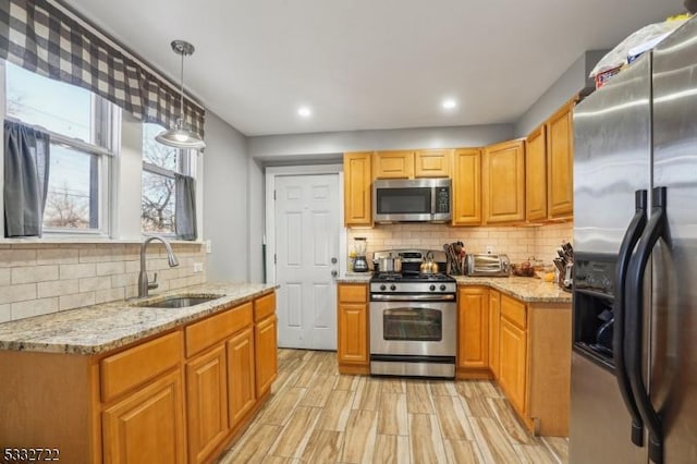 kitchen featuring sink, backsplash, light stone countertops, pendant lighting, and appliances with stainless steel finishes