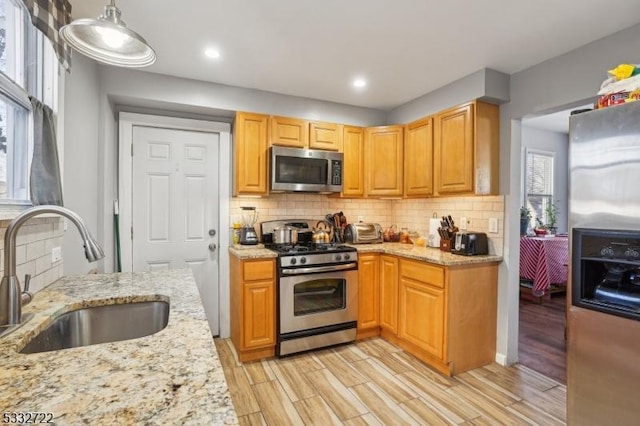 kitchen with decorative light fixtures, stainless steel appliances, light stone countertops, and sink