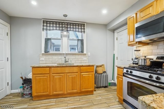 kitchen with decorative light fixtures, backsplash, appliances with stainless steel finishes, radiator heating unit, and sink