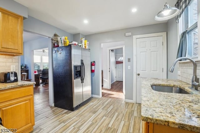 kitchen featuring sink, light hardwood / wood-style flooring, decorative backsplash, stainless steel fridge with ice dispenser, and light stone countertops