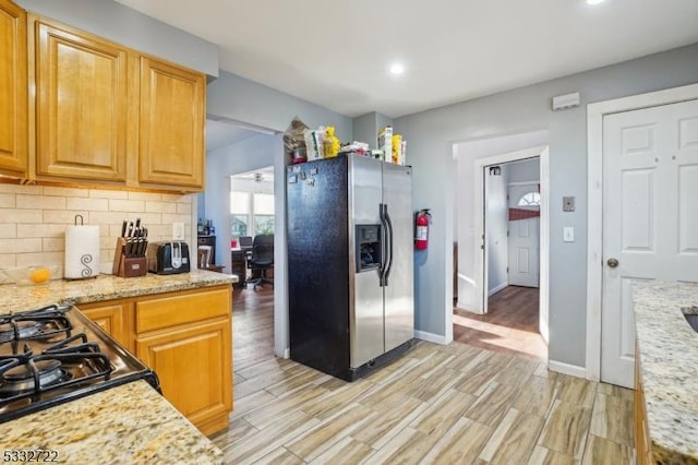 kitchen featuring light stone counters, light wood-type flooring, stainless steel refrigerator with ice dispenser, and decorative backsplash