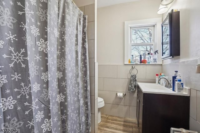 bathroom featuring curtained shower, tile walls, toilet, wood-type flooring, and vanity