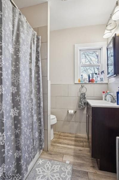 bathroom featuring toilet, hardwood / wood-style flooring, tile walls, a shower with curtain, and vanity