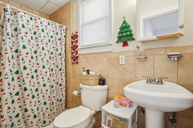 bathroom with toilet, a drop ceiling, tile walls, a shower with shower curtain, and sink