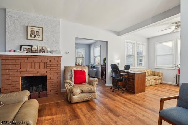 office featuring a fireplace, beamed ceiling, hardwood / wood-style floors, ceiling fan, and radiator