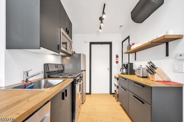 kitchen with wooden counters, rail lighting, stainless steel appliances, sink, and light hardwood / wood-style flooring