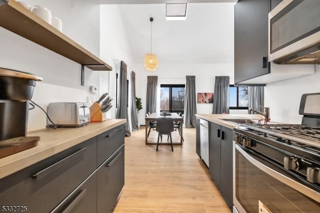 kitchen with stainless steel appliances, sink, light hardwood / wood-style flooring, butcher block countertops, and pendant lighting