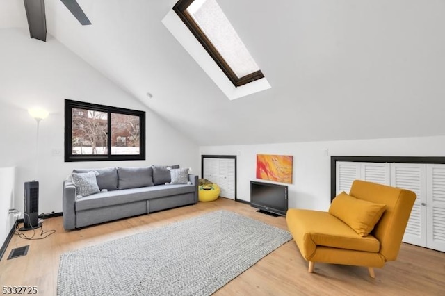 living area with vaulted ceiling with skylight and hardwood / wood-style floors