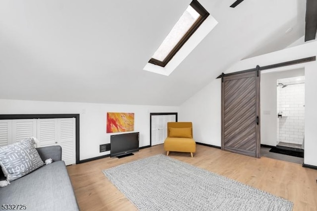 interior space featuring hardwood / wood-style floors, lofted ceiling with skylight, and a barn door