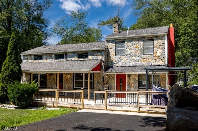 view of front of property featuring covered porch, a chimney, and stone siding