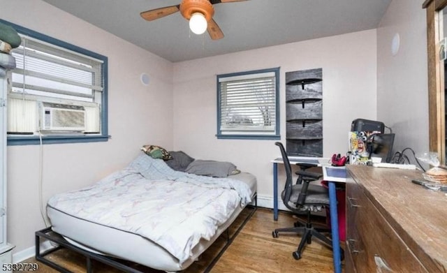 bedroom with ceiling fan, cooling unit, multiple windows, and hardwood / wood-style flooring