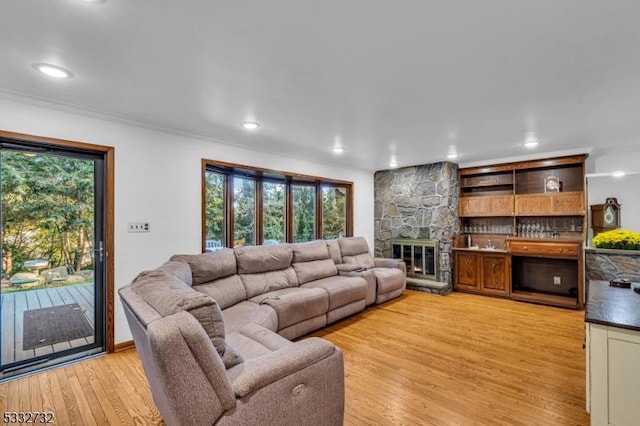 living room featuring a stone fireplace, crown molding, and light hardwood / wood-style floors