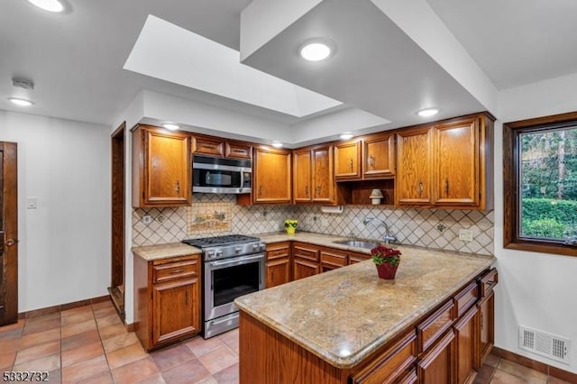 kitchen featuring kitchen peninsula, light stone countertops, tasteful backsplash, stainless steel appliances, and sink