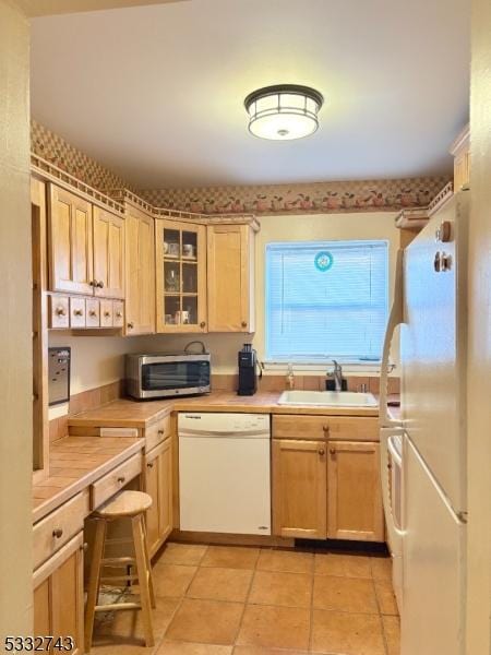 kitchen featuring light brown cabinetry, sink, white appliances, and light tile patterned floors