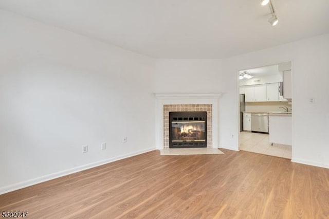 unfurnished living room featuring ceiling fan, a tile fireplace, sink, light wood-type flooring, and rail lighting